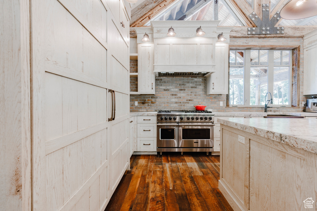 Kitchen with double oven range, dark wood-style flooring, backsplash, light stone counters, and white cabinetry