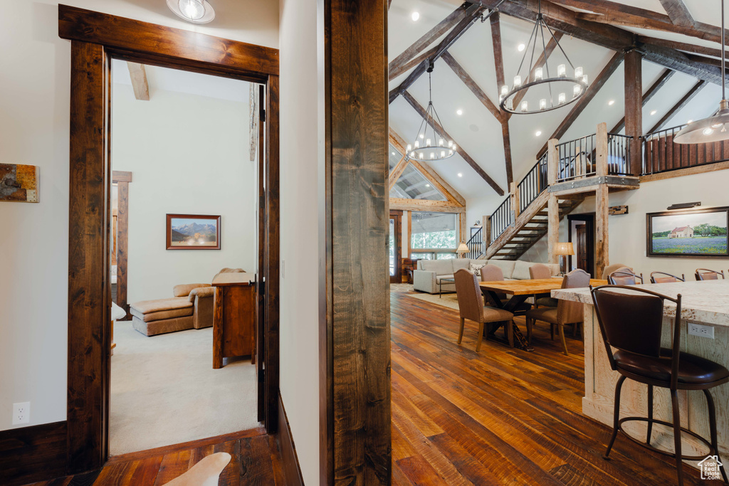Hallway with beam ceiling, stairway, wood-type flooring, high vaulted ceiling, and a chandelier