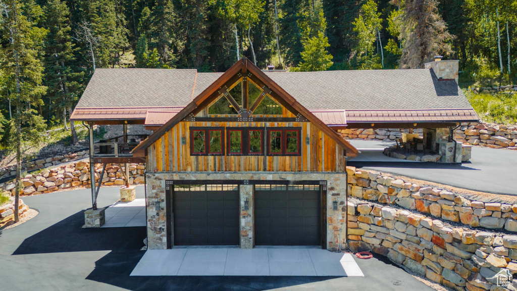 View of front facade featuring a chimney, stone siding, a garage, a wooded view, and driveway