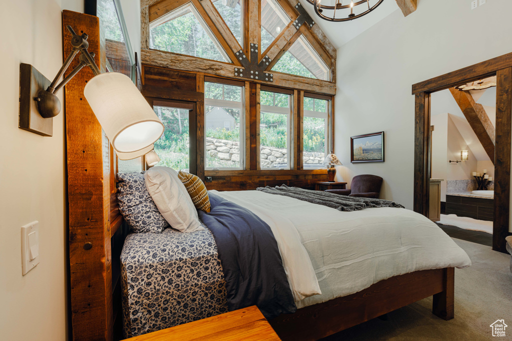 Carpeted bedroom featuring high vaulted ceiling, beamed ceiling, a chandelier, and ensuite bathroom