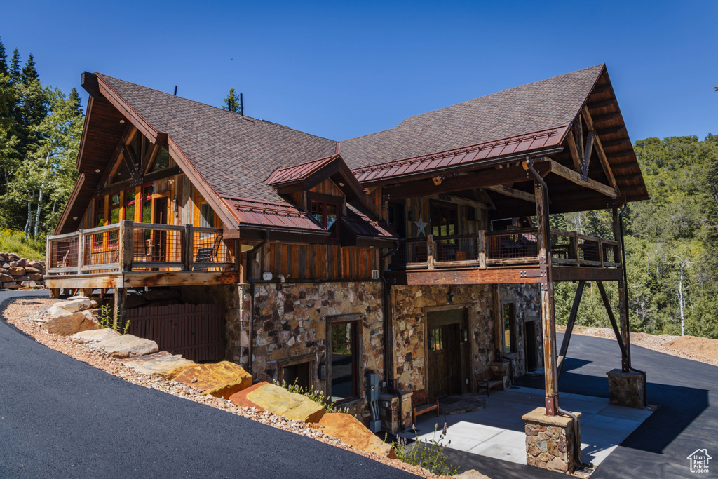 View of front facade featuring a standing seam roof, board and batten siding, a balcony, roof with shingles, and a metal roof