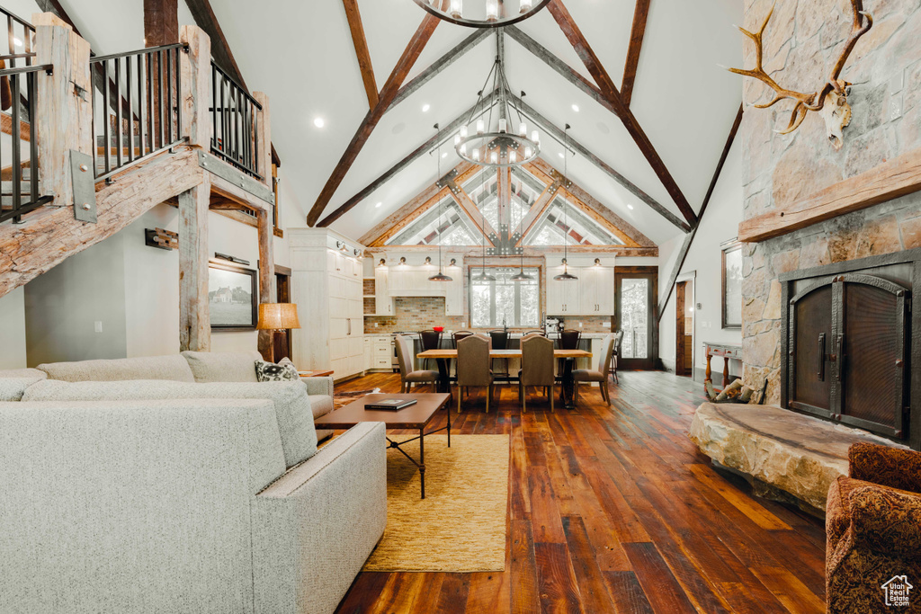 Living area featuring a chandelier, hardwood / wood-style floors, a stone fireplace, beam ceiling, and high vaulted ceiling