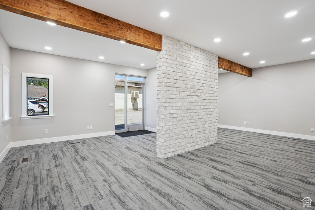 Unfurnished living room featuring healthy amount of natural light, wood finished floors, recessed lighting, and beamed ceiling