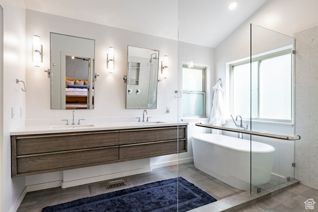 Full bathroom featuring connected bathroom, double vanity, a soaking tub, and vaulted ceiling