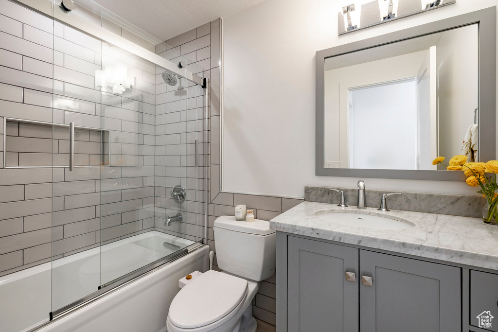 Bathroom featuring vanity, bath / shower combo with glass door, and tile walls
