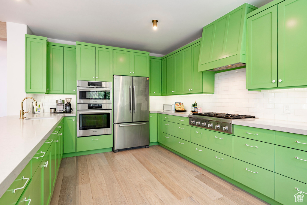 Kitchen with stainless steel appliances, light wood-style floors, tasteful backsplash, and light countertops