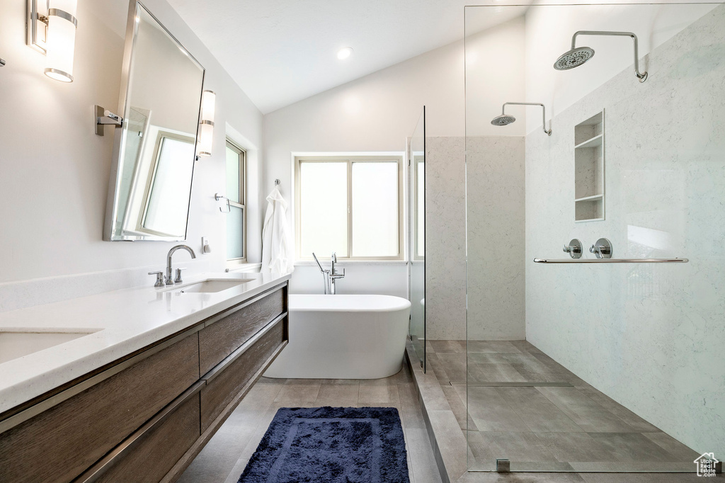 Bathroom with vaulted ceiling, a walk in shower, double vanity, a freestanding bath, and tile patterned flooring