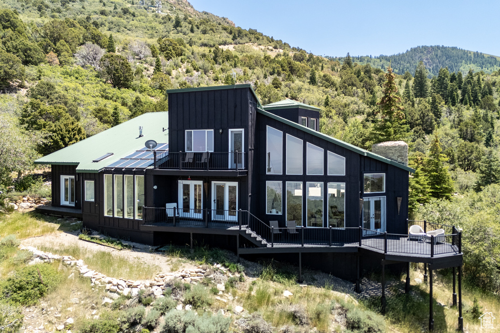Rear view of property with french doors, a forest view, a deck, and a chimney