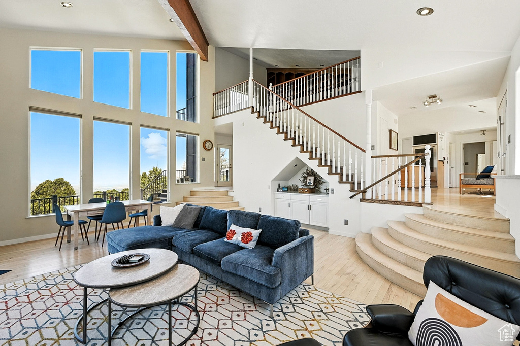 Living area featuring stairs, light wood finished floors, a towering ceiling, beam ceiling, and recessed lighting