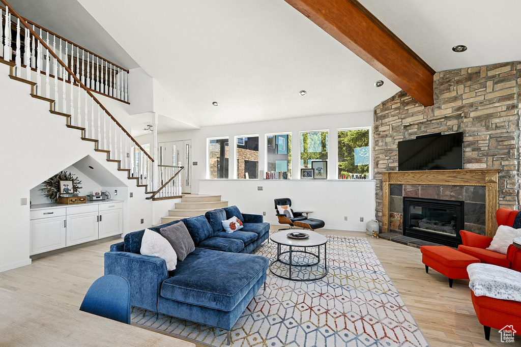 Living room featuring light wood finished floors, stairs, high vaulted ceiling, beam ceiling, and a fireplace