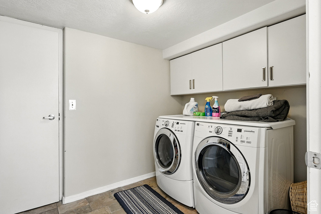 Laundry area with washing machine and clothes dryer, cabinet space, and light stone finish flooring