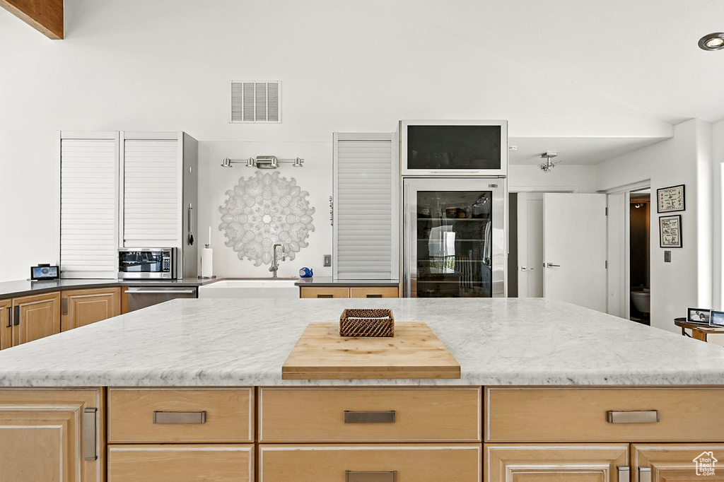 Kitchen with beverage cooler, appliances with stainless steel finishes, light stone countertops, a kitchen island, and high vaulted ceiling