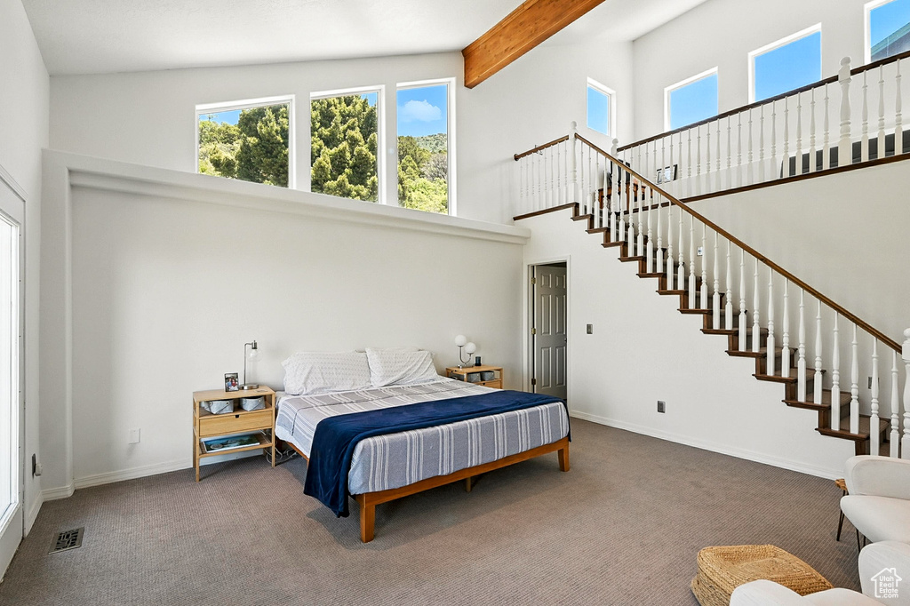Carpeted bedroom with a towering ceiling, multiple windows, and beam ceiling