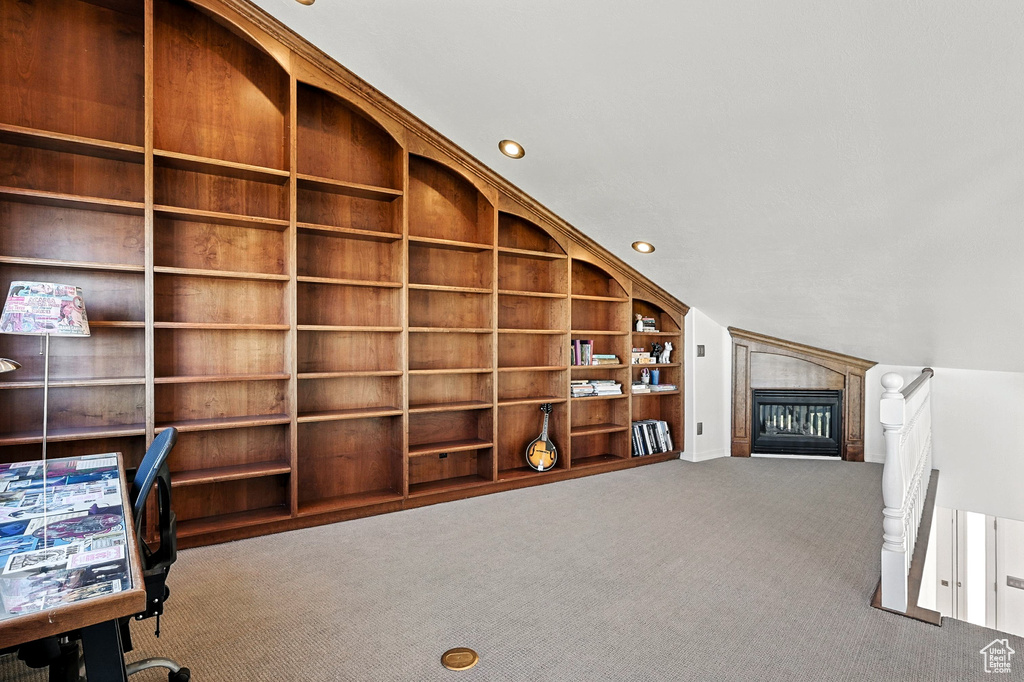 Unfurnished office with carpet, a tiled fireplace, built in shelves, vaulted ceiling, and recessed lighting