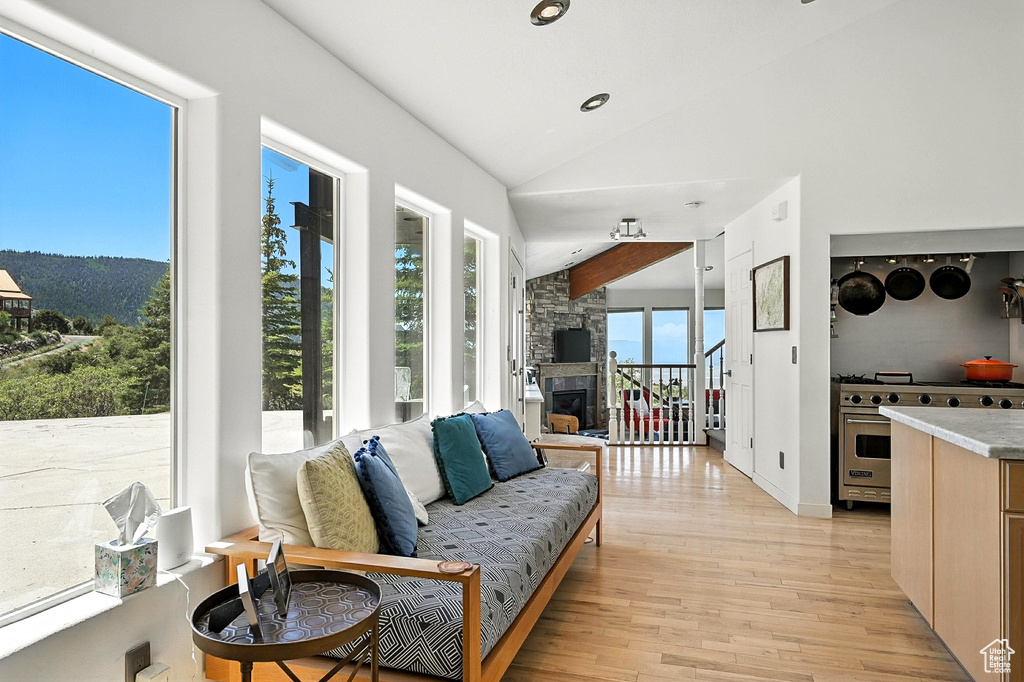 Living area with lofted ceiling, light wood finished floors, and a stone fireplace
