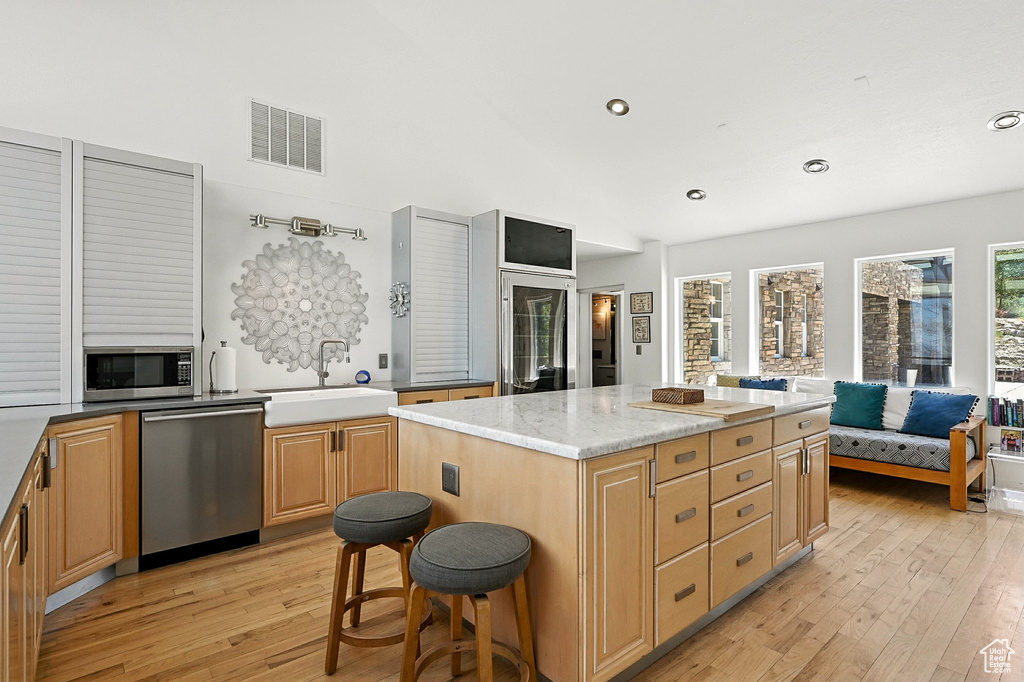 Kitchen with stainless steel appliances, light wood-style flooring, recessed lighting, a kitchen island, and light stone countertops
