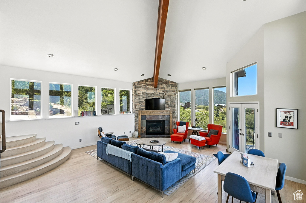 Living room featuring beam ceiling, a stone fireplace, light wood-type flooring, healthy amount of natural light, and french doors