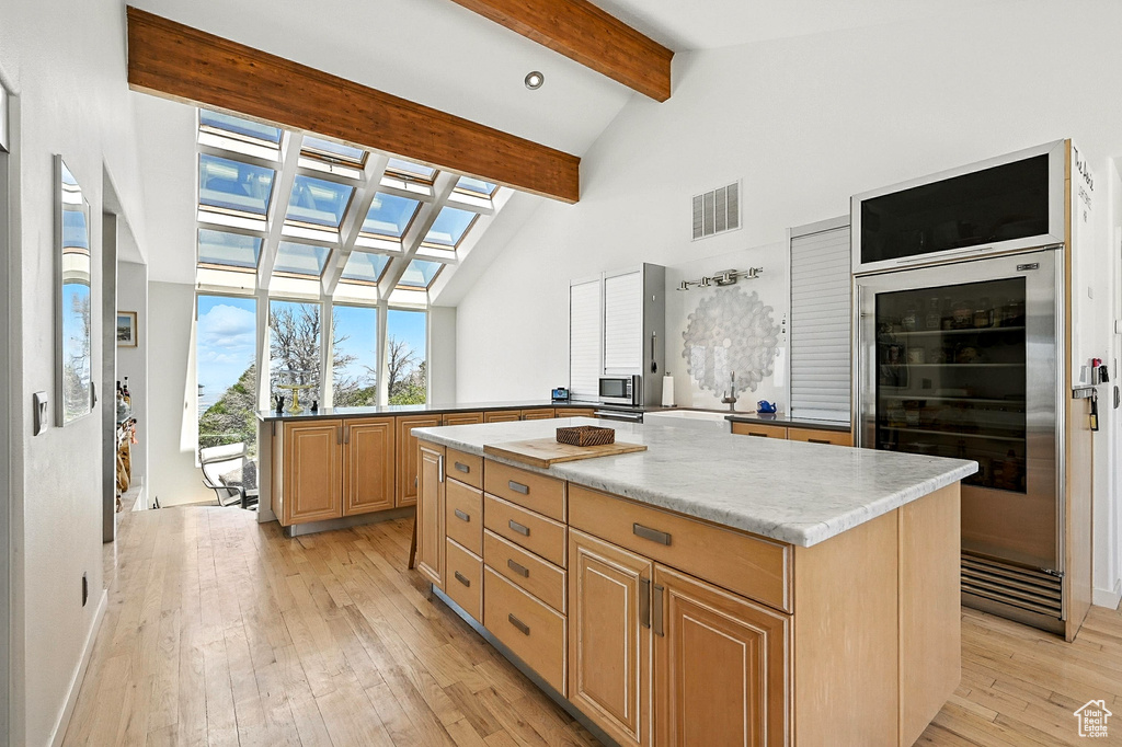 Kitchen with beverage cooler, beam ceiling, light wood-style floors, light brown cabinetry, and high vaulted ceiling