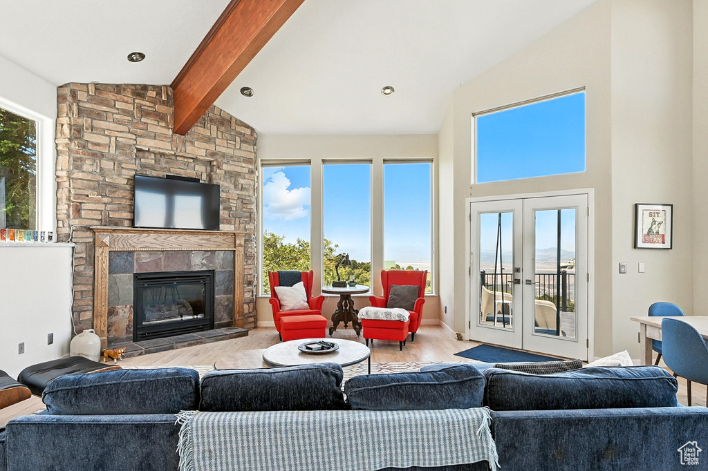 Living room with french doors, beam ceiling, wood finished floors, a stone fireplace, and high vaulted ceiling