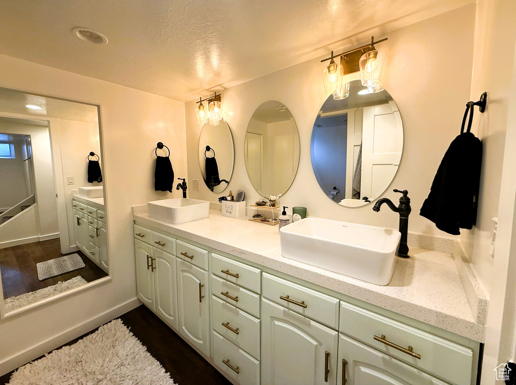 Bathroom with double vanity, wood finished floors, and a textured ceiling