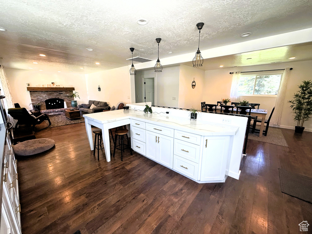 Kitchen featuring a textured ceiling, a kitchen breakfast bar, open floor plan, white cabinetry, and a brick fireplace