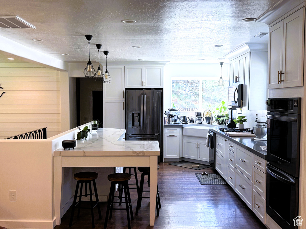Kitchen featuring fridge with ice dispenser, a breakfast bar area, dark wood-style flooring, decorative light fixtures, and a textured ceiling