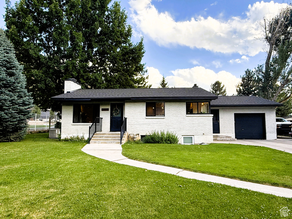 View of front of home with a chimney, a garage, brick siding, a front lawn, and driveway
