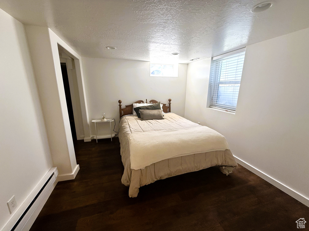 Bedroom featuring a baseboard heating unit, a textured ceiling, and wood finished floors
