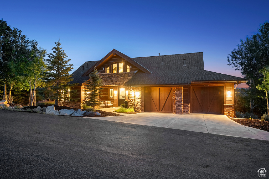 View of front facade with concrete driveway, stone siding, a shingled roof, and an attached garage