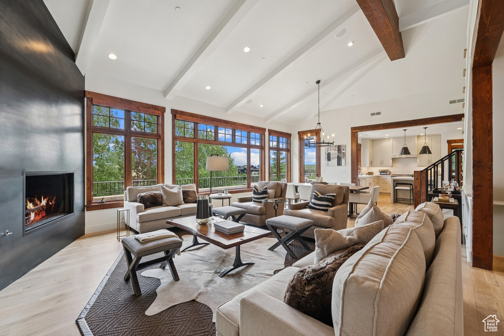 Living room featuring a fireplace, beamed ceiling, light wood finished floors, a chandelier, and high vaulted ceiling