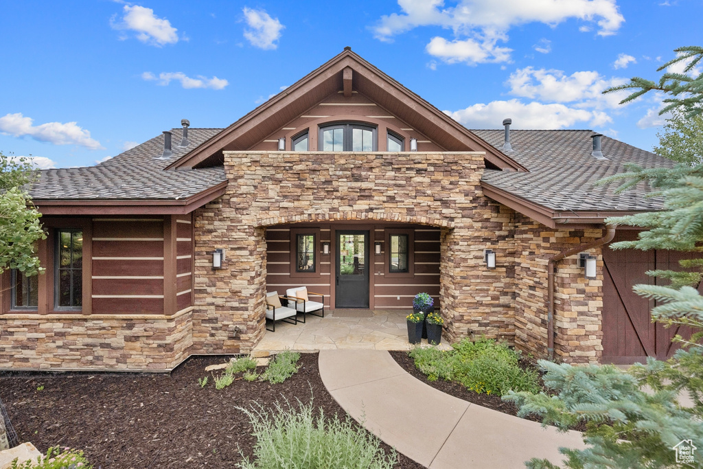 View of front of house featuring stone siding and a shingled roof