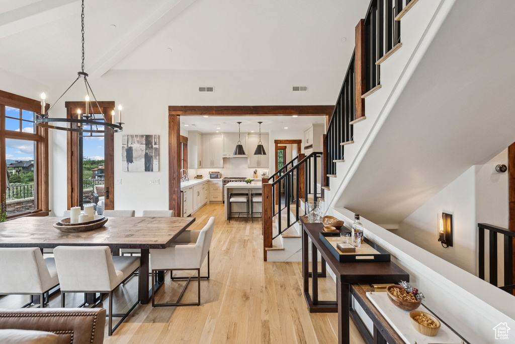 Dining room with light wood finished floors, a chandelier, stairs, and beamed ceiling