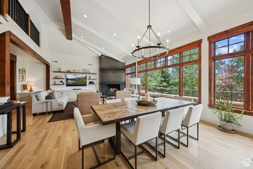 Dining area featuring beam ceiling, light wood-style flooring, high vaulted ceiling, a chandelier, and a fireplace