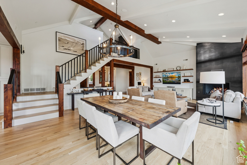 Dining room with light wood-style floors, stairs, beamed ceiling, a large fireplace, and high vaulted ceiling
