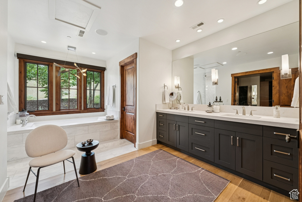 Bathroom featuring a garden tub, double vanity, wood finished floors, and recessed lighting