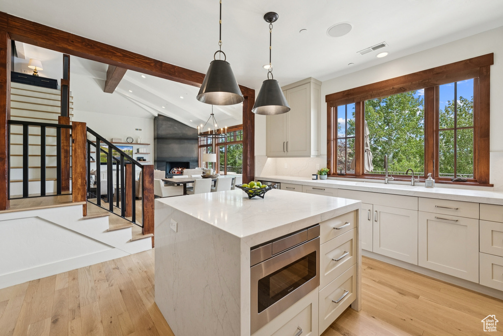 Kitchen with stainless steel microwave, healthy amount of natural light, recessed lighting, light wood finished floors, and hanging light fixtures