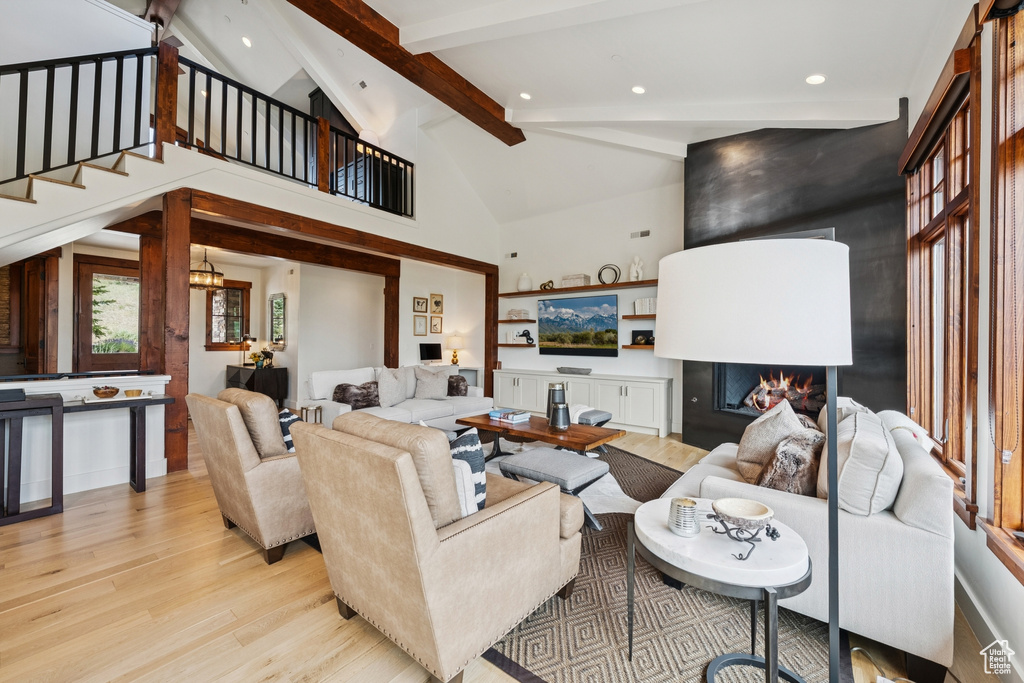 Living area with light wood-style floors, a lit fireplace, beamed ceiling, recessed lighting, and high vaulted ceiling