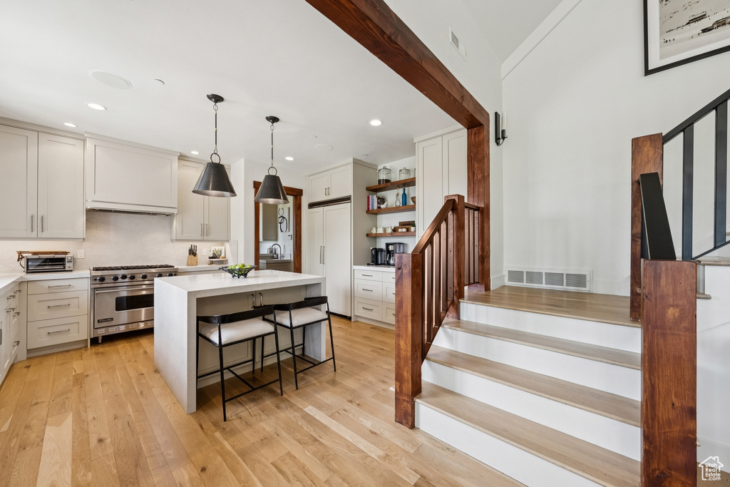 Kitchen with high end appliances, open shelves, light countertops, a kitchen breakfast bar, and light wood finished floors