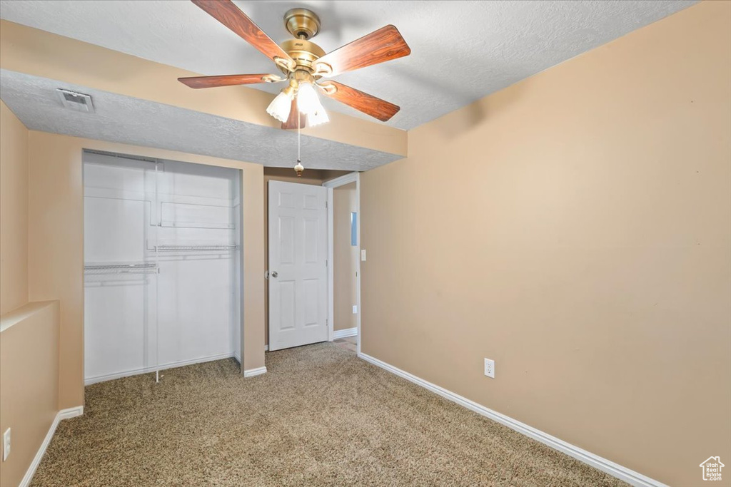 Unfurnished bedroom featuring a closet, carpet floors, a textured ceiling, and ceiling fan