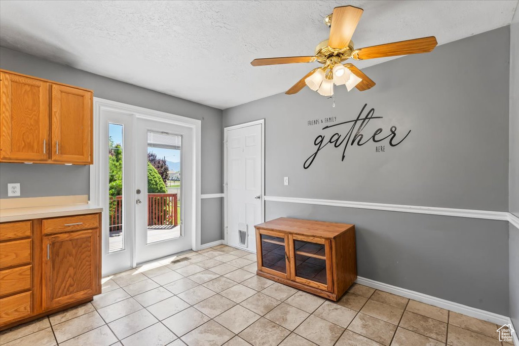 Doorway to outside with a ceiling fan, light tile patterned flooring, and a textured ceiling