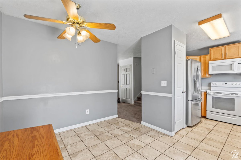 Kitchen with white appliances, light tile patterned floors, and a ceiling fan