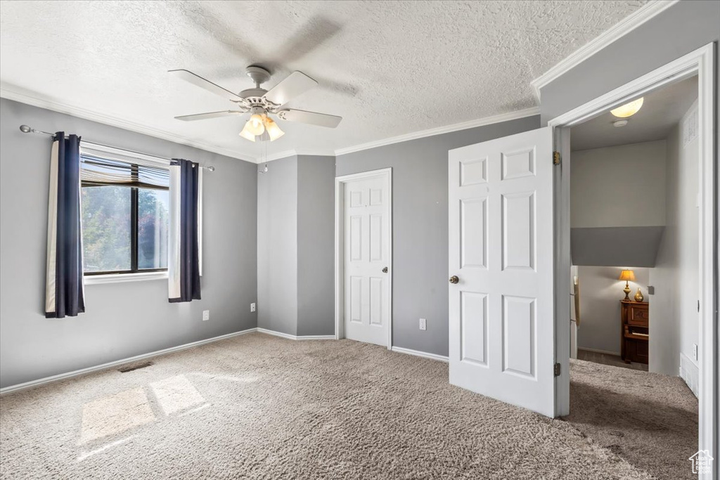 Unfurnished bedroom with a textured ceiling, carpet flooring, ornamental molding, and a ceiling fan