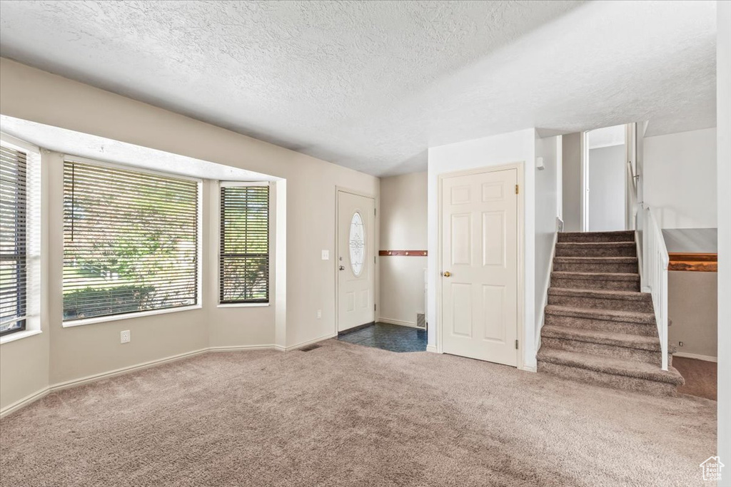 Unfurnished living room with carpet flooring, a textured ceiling, and stairs