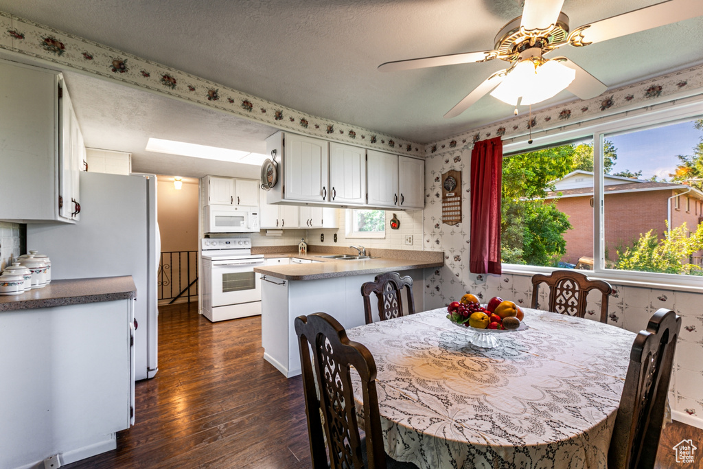 Kitchen with white appliances, dark wood-type flooring, a peninsula, white cabinets, and wallpapered walls