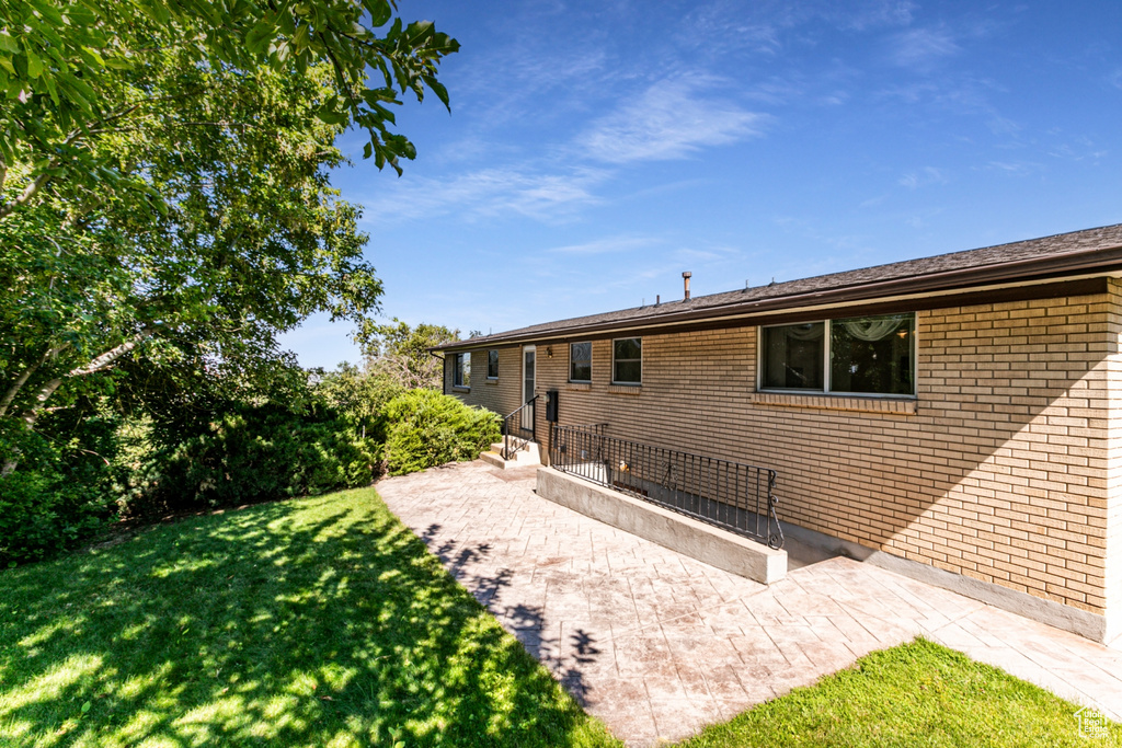 Back of house featuring a yard, brick siding, and a patio area