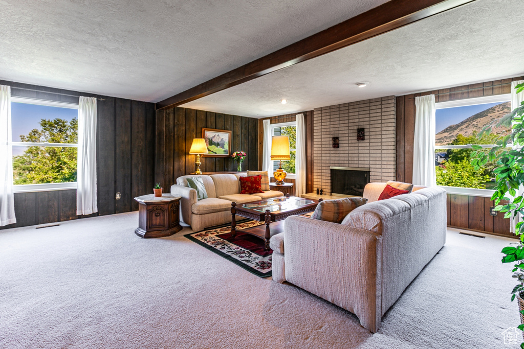 Living area with a textured ceiling, carpet, plenty of natural light, a brick fireplace, and beamed ceiling