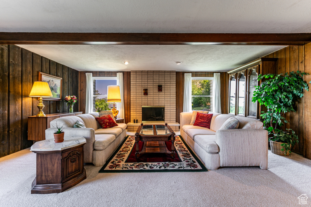 Living area featuring beamed ceiling, wood walls, carpet floors, a brick fireplace, and a textured ceiling