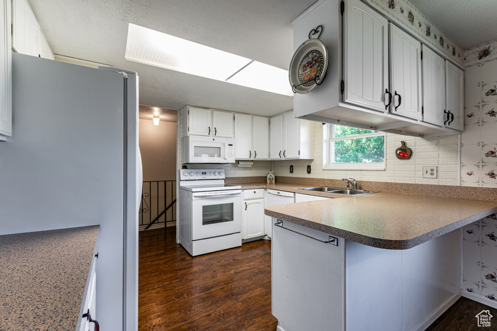 Kitchen with white appliances, a peninsula, dark wood finished floors, decorative backsplash, and white cabinets