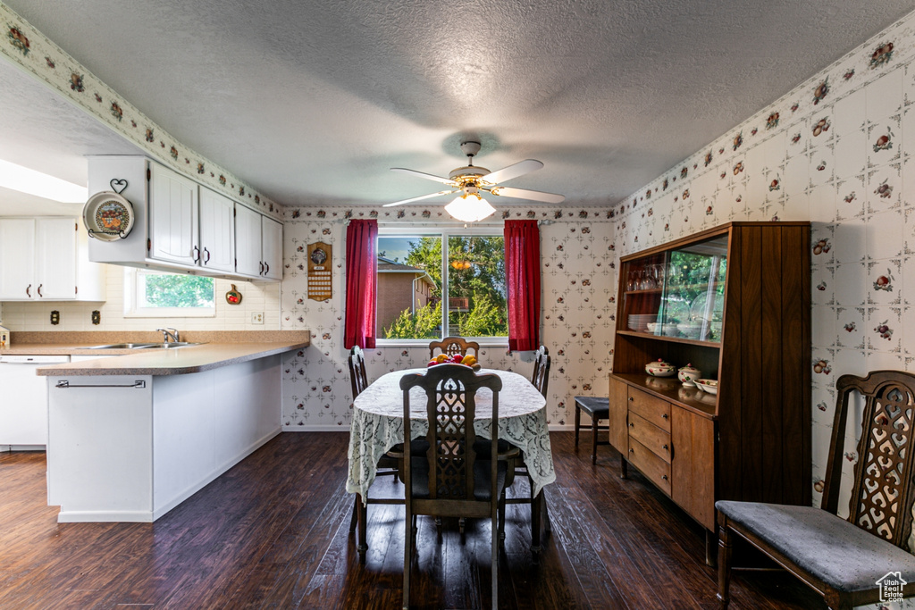 Dining area featuring wallpapered walls, dark wood-type flooring, ceiling fan, and a textured ceiling