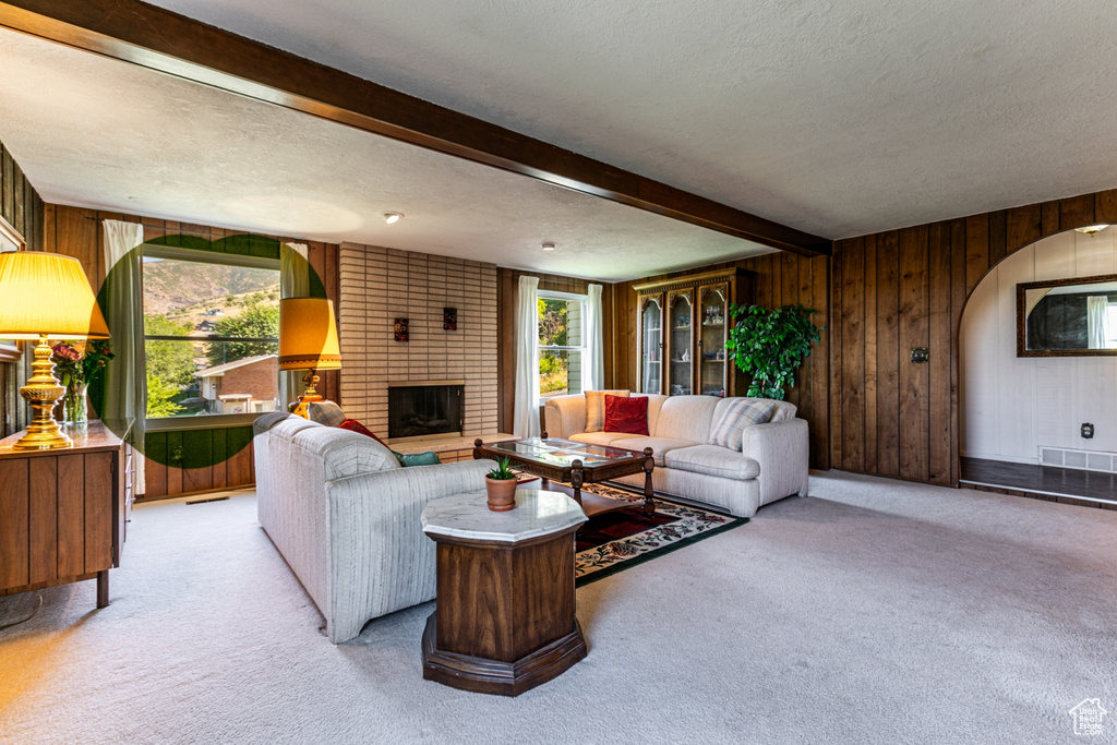 Living room with light colored carpet, beamed ceiling, a textured ceiling, wooden walls, and a brick fireplace